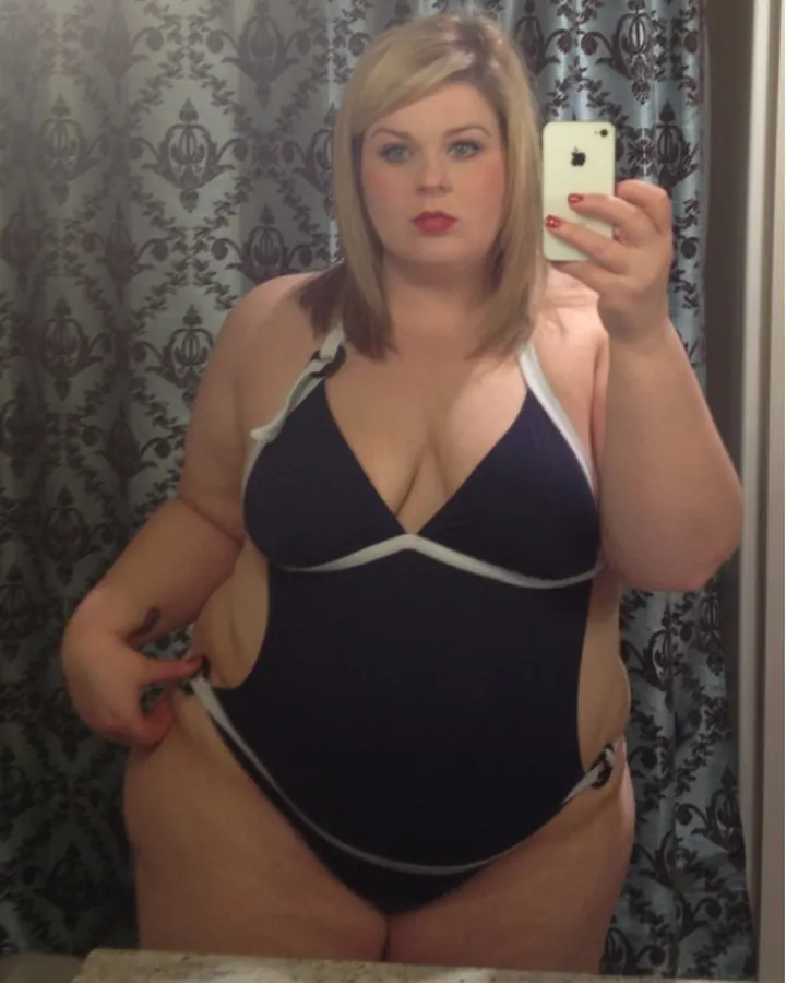 Femme ronde aux cheveux blonds devant un miroir, maillot de bain noir et blanc