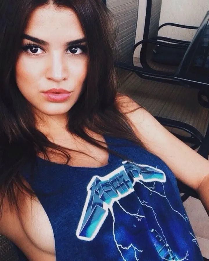 Jeune femme brune en débardeur bleu, assise près d'une table en verre, lumière du jour.