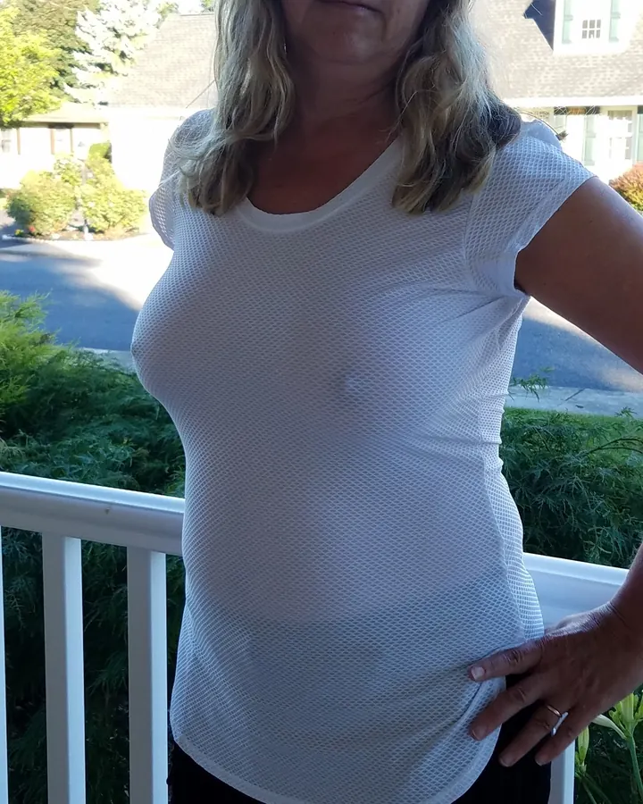 Femme aux cheveux gris en tenue claire devant un mur rouge vif