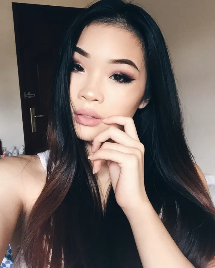 Jeune femme asiatique aux longs cheveux noirs, main près du visage, regard caméra.
