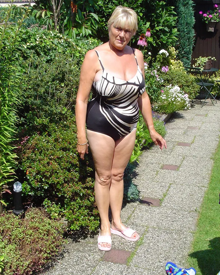 Femme blonde en maillot noir et blanc dans un jardin, allée de gravier, lumière du jour.