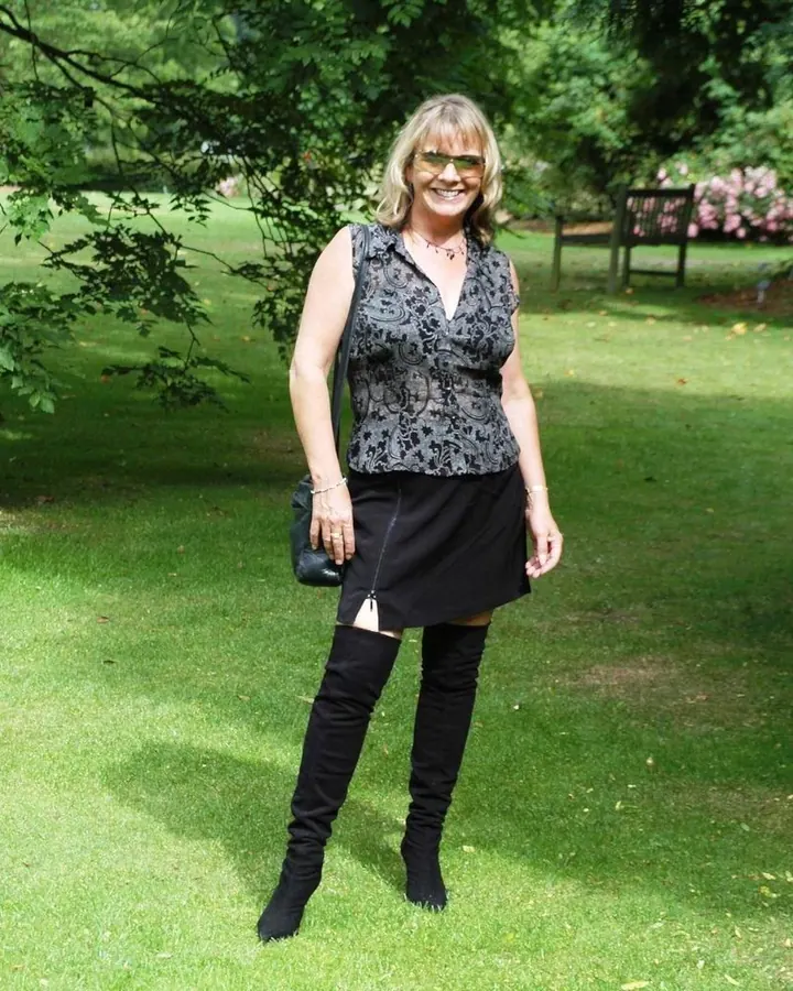 Femme aux cheveux platine et lunettes de soleil, robe noire, bottes hautes, dans un parc ensoleillé