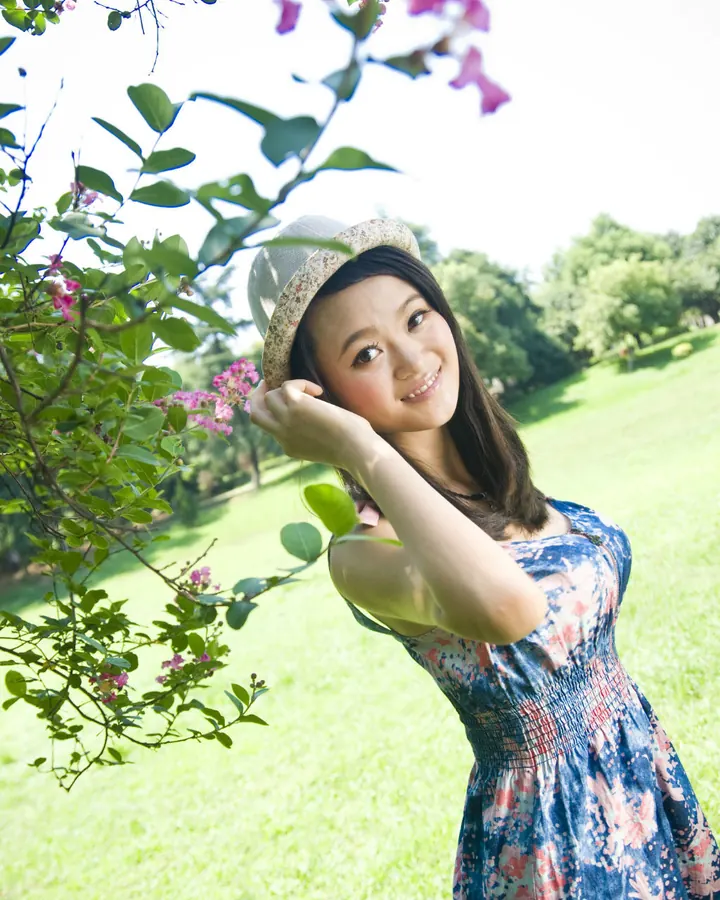 Femme asiatique, chapeau clair, robe fleurie bleue, dans un jardin ensoleillé