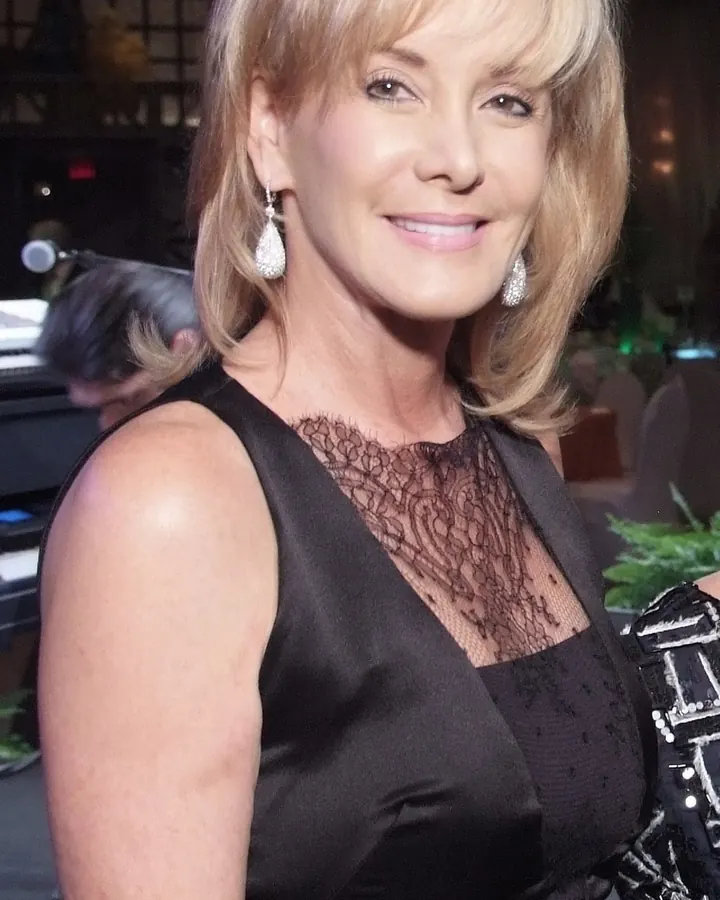 Femme blonde platine en tenue de cuir noir, debout dans une pièce claire.