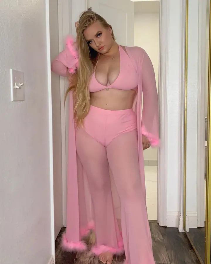 Femme ronde en ensemble rose, robe transparente bordée de plumes, couloir clair