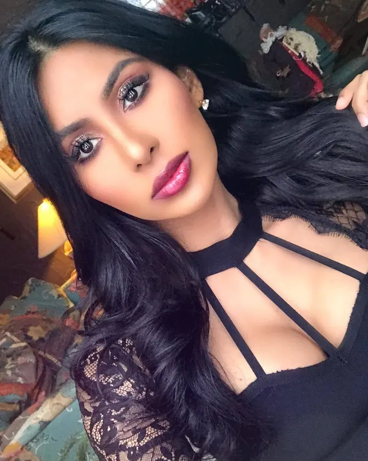 Jeune femme aux longs cheveux noirs, haut noir à lacets, selfie en intérieur, regard direct
