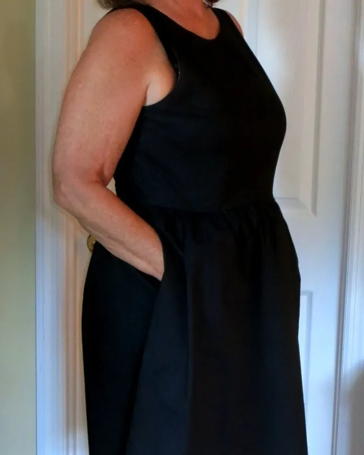 Femme aux cheveux courts, lunettes, robe sombre, debout devant une porte blanche