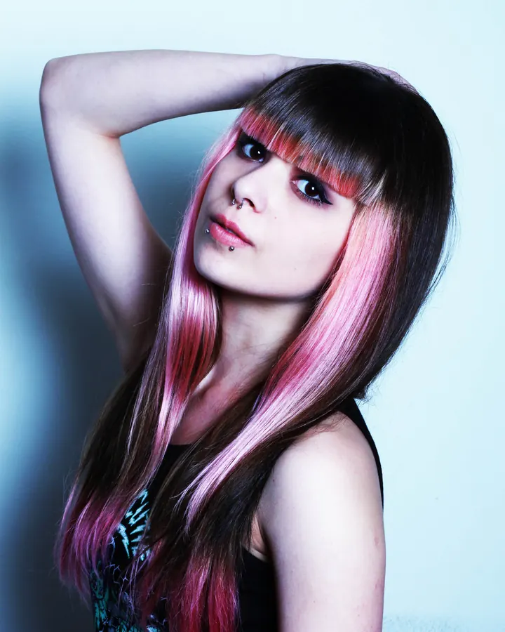 Femme aux cheveux roses, frange droite, piercing au nez, fond bleu pâle
